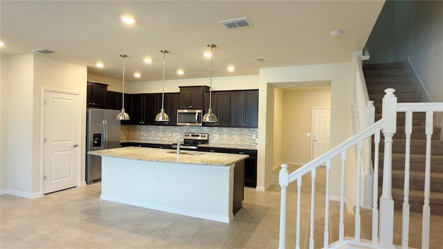 kitchen featuring sink, a kitchen island with sink, backsplash, stainless steel appliances, and light stone countertops