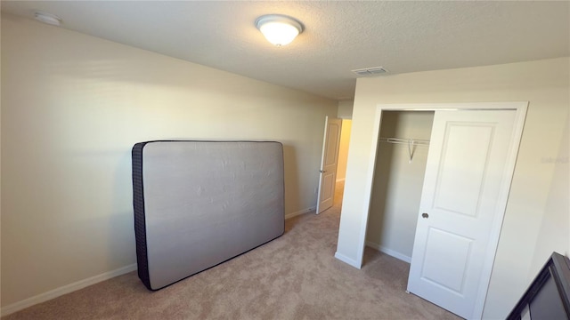 unfurnished bedroom with light colored carpet, a textured ceiling, and a closet