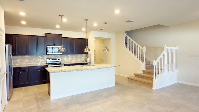 kitchen featuring sink, light stone counters, hanging light fixtures, appliances with stainless steel finishes, and an island with sink