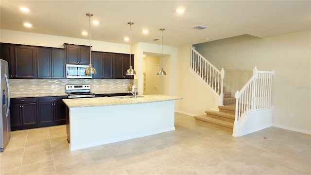 kitchen featuring decorative light fixtures, tasteful backsplash, light stone counters, stainless steel appliances, and a center island with sink