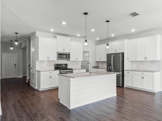 kitchen featuring pendant lighting, sink, appliances with stainless steel finishes, white cabinets, and a center island with sink