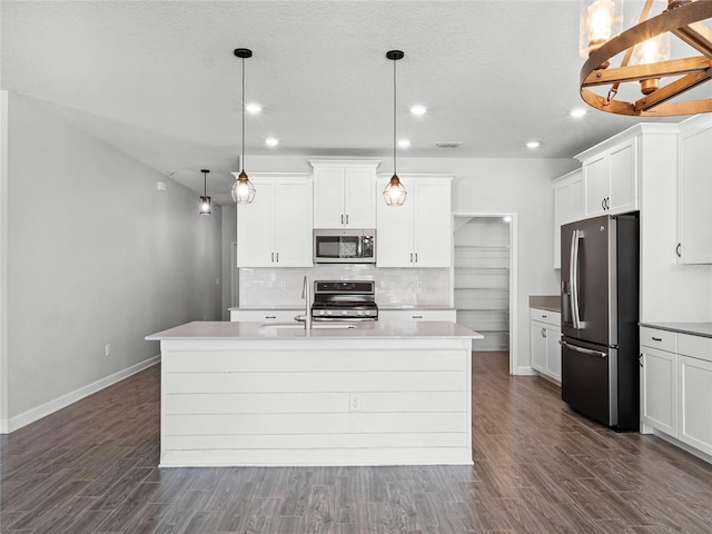 kitchen featuring an island with sink, appliances with stainless steel finishes, pendant lighting, and white cabinets