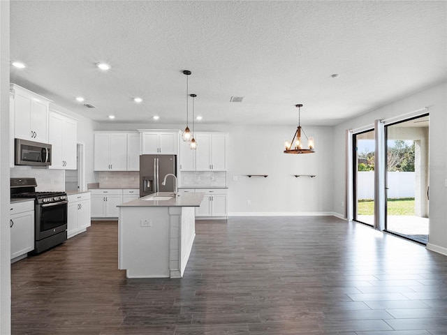 kitchen featuring white cabinets, backsplash, hanging light fixtures, stainless steel appliances, and a center island with sink