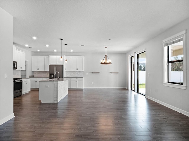 kitchen with white cabinetry, hanging light fixtures, backsplash, stainless steel appliances, and a center island with sink