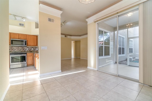 interior space featuring appliances with stainless steel finishes, backsplash, track lighting, ornamental molding, and light tile patterned flooring