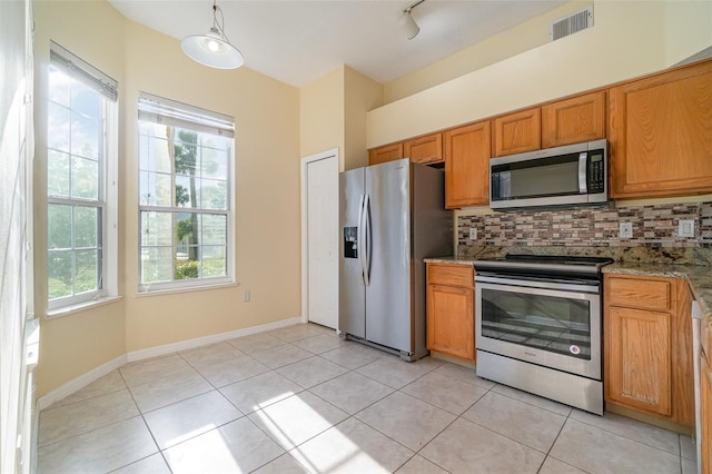 kitchen with light stone countertops, appliances with stainless steel finishes, light tile patterned floors, and backsplash