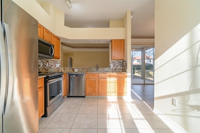 kitchen with light stone counters, stainless steel appliances, tasteful backsplash, light tile patterned flooring, and a sink