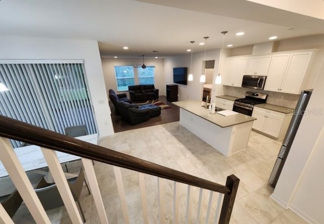 kitchen with pendant lighting, white cabinets, backsplash, a kitchen island with sink, and stainless steel appliances