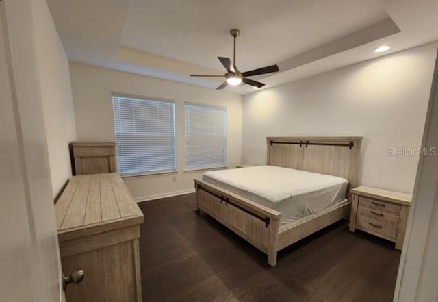 bedroom with a raised ceiling, dark wood-type flooring, and ceiling fan