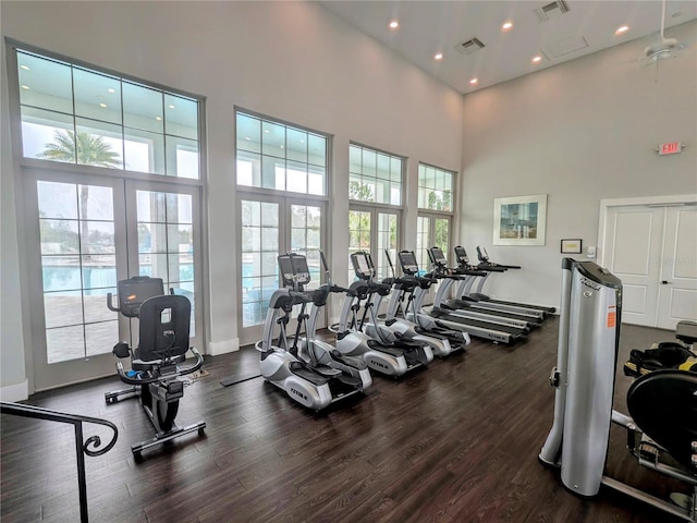 gym with a wealth of natural light, dark wood-type flooring, and a towering ceiling