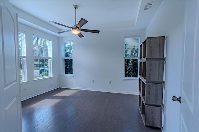 spare room with ceiling fan, dark wood-type flooring, visible vents, baseboards, and a tray ceiling