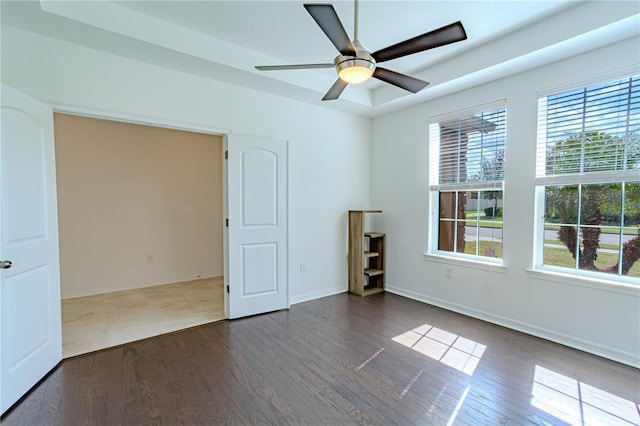 unfurnished room with plenty of natural light, a tray ceiling, ceiling fan, and wood finished floors