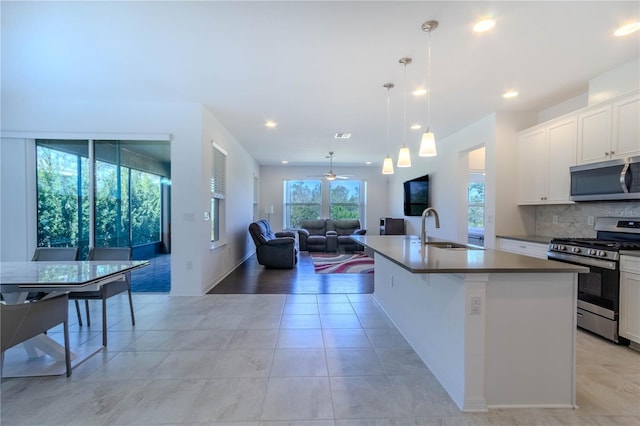 kitchen featuring a kitchen island with sink, a sink, open floor plan, appliances with stainless steel finishes, and backsplash