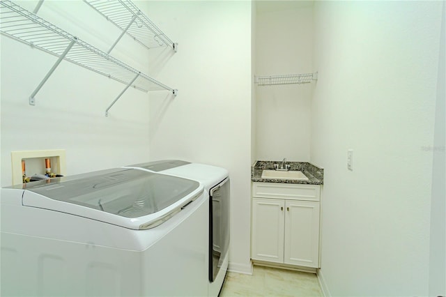 clothes washing area with cabinet space, washing machine and dryer, baseboards, and a sink