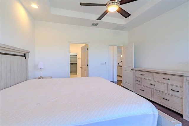 bedroom featuring visible vents, a ceiling fan, dark wood-style flooring, a spacious closet, and a tray ceiling