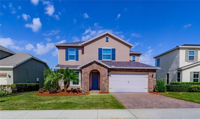 traditional-style home featuring decorative driveway, stucco siding, a front yard, a garage, and stone siding