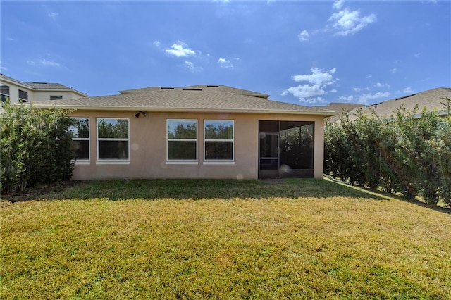 back of house with a shingled roof, a sunroom, a lawn, and stucco siding