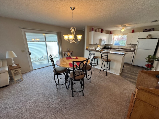 carpeted dining space with sink, ceiling fan with notable chandelier, and a textured ceiling