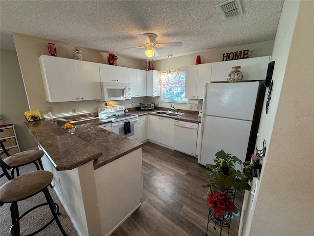 kitchen featuring sink, white appliances, white cabinetry, a kitchen bar, and kitchen peninsula