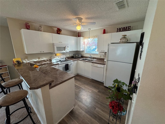 482 Hildalgo Dr, The Villages, FL 32159 - kitchen with white appliances, a sink, a peninsula, dark countertops, and white cabinetry
