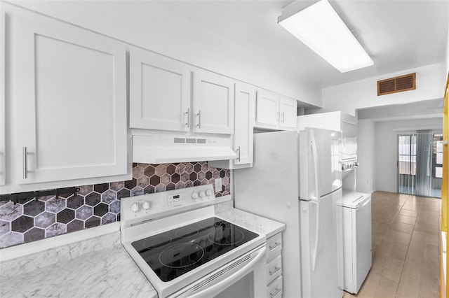 kitchen with stacked washer and dryer, white appliances, white cabinetry, backsplash, and light stone counters