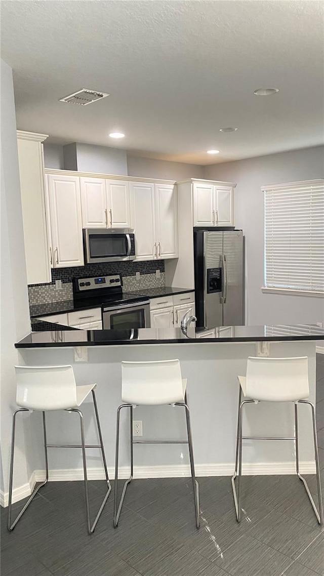 kitchen featuring white cabinetry, backsplash, a kitchen breakfast bar, kitchen peninsula, and stainless steel appliances