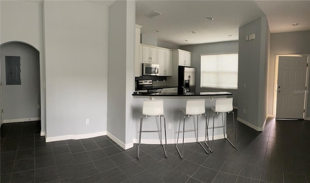 kitchen featuring a breakfast bar, appliances with stainless steel finishes, electric panel, tasteful backsplash, and white cabinets