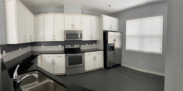 kitchen featuring sink, appliances with stainless steel finishes, dark tile patterned flooring, decorative backsplash, and white cabinets