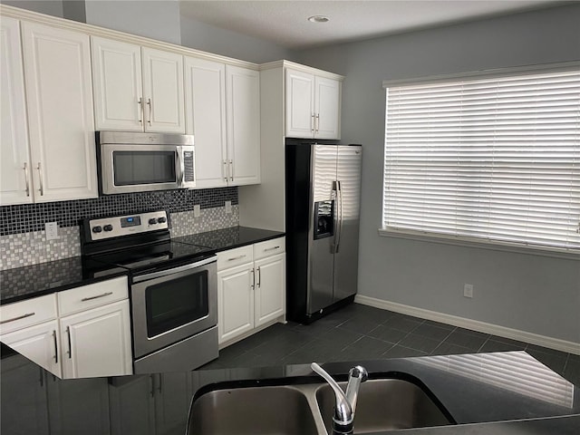 kitchen featuring sink, white cabinetry, stainless steel appliances, tasteful backsplash, and dark tile patterned flooring