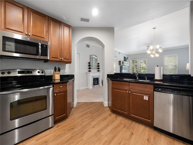 kitchen with stainless steel appliances, sink, an inviting chandelier, light wood-type flooring, and a high end fireplace