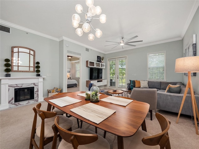 carpeted dining room featuring ceiling fan with notable chandelier, a high end fireplace, ornamental molding, and french doors