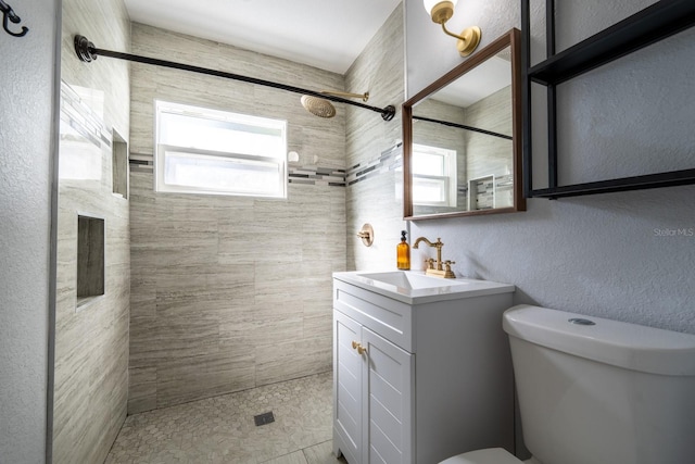 bathroom featuring vanity, a tile shower, and toilet