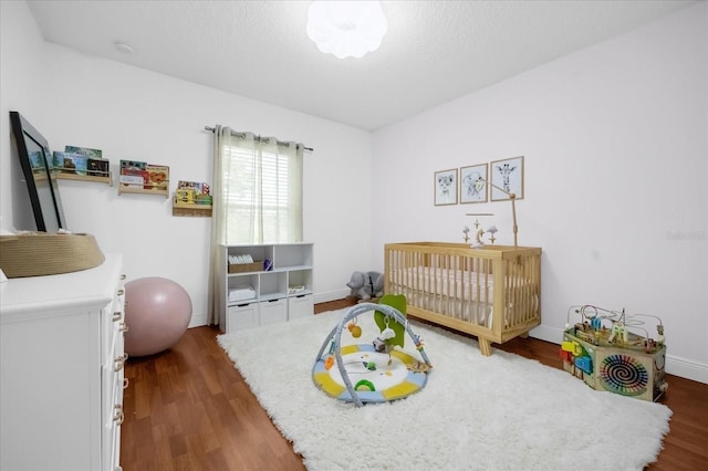 bedroom featuring dark hardwood / wood-style flooring, a nursery area, and a textured ceiling