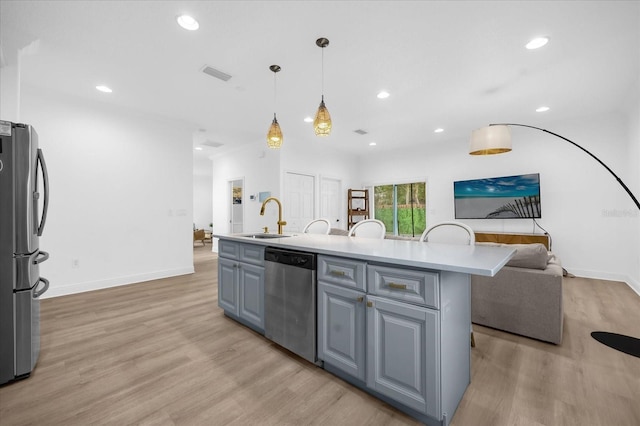 kitchen with sink, gray cabinets, appliances with stainless steel finishes, hanging light fixtures, and a center island with sink