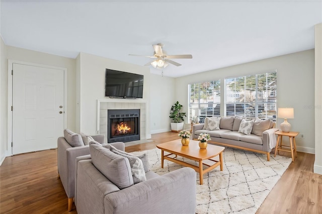 living area featuring a tile fireplace, wood finished floors, a ceiling fan, and baseboards