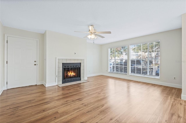 unfurnished living room featuring ceiling fan, a tiled fireplace, wood finished floors, and baseboards