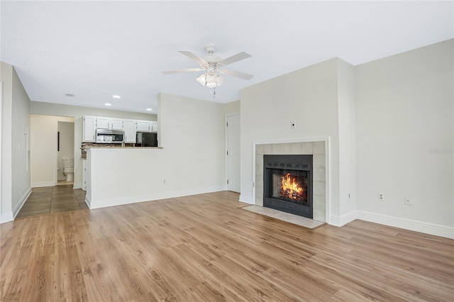 unfurnished living room with light wood-style floors, a tile fireplace, ceiling fan, and baseboards