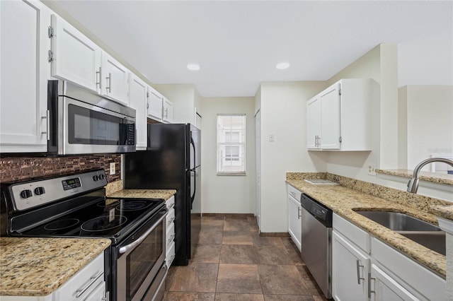 kitchen featuring tasteful backsplash, white cabinets, stone finish floor, stainless steel appliances, and a sink