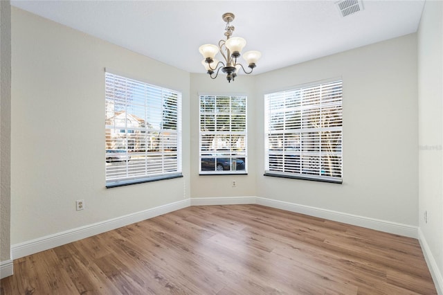 unfurnished dining area featuring visible vents, baseboards, a notable chandelier, and wood finished floors