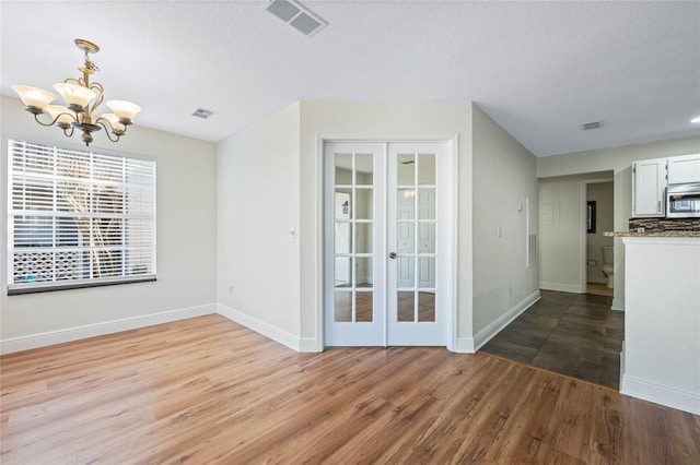 unfurnished room featuring french doors, visible vents, an inviting chandelier, and wood finished floors