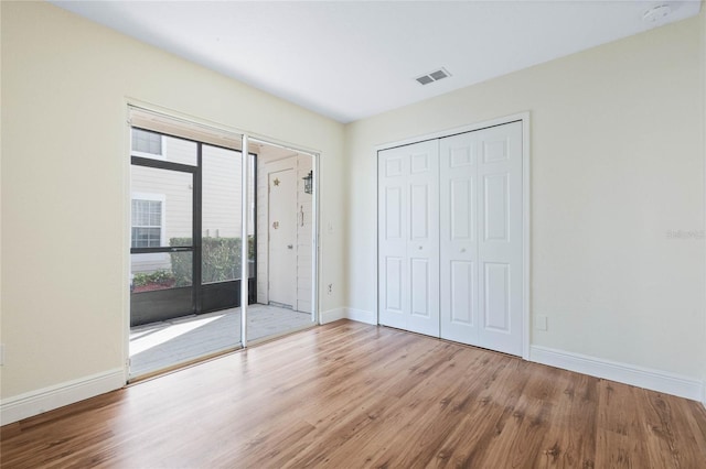 unfurnished bedroom featuring wood finished floors, visible vents, baseboards, access to outside, and a closet