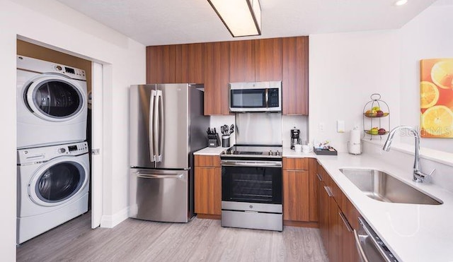 kitchen featuring sink, light wood-type flooring, stacked washer and clothes dryer, and appliances with stainless steel finishes