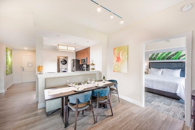 dining area with stacked washer / dryer, rail lighting, and light hardwood / wood-style floors