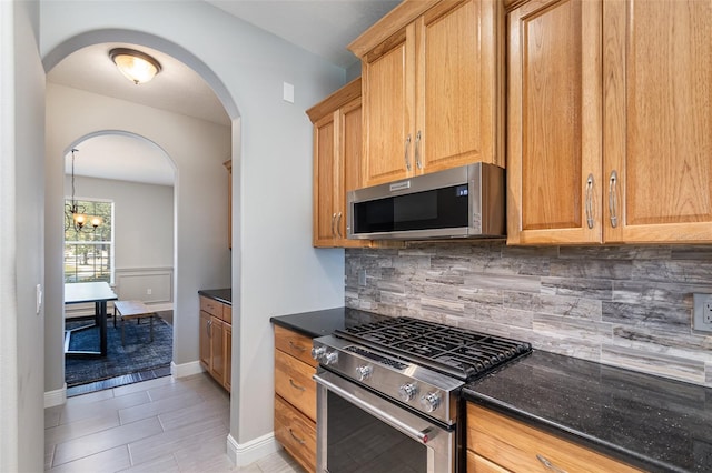 kitchen featuring stainless steel appliances, a chandelier, decorative backsplash, and dark stone counters