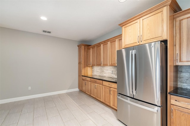 kitchen with light brown cabinetry, backsplash, and stainless steel refrigerator