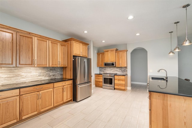 kitchen with sink, appliances with stainless steel finishes, a kitchen island with sink, hanging light fixtures, and decorative backsplash