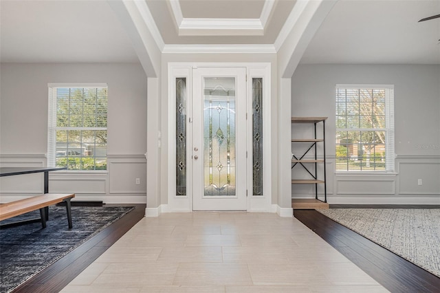 entryway featuring a raised ceiling, crown molding, plenty of natural light, and light wood-type flooring