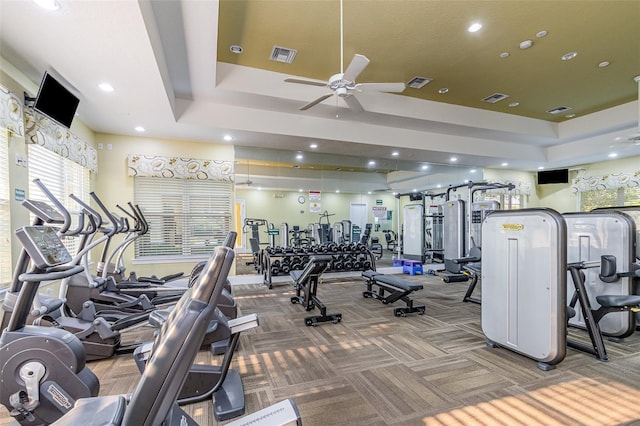 workout area featuring ceiling fan, carpet flooring, and a tray ceiling