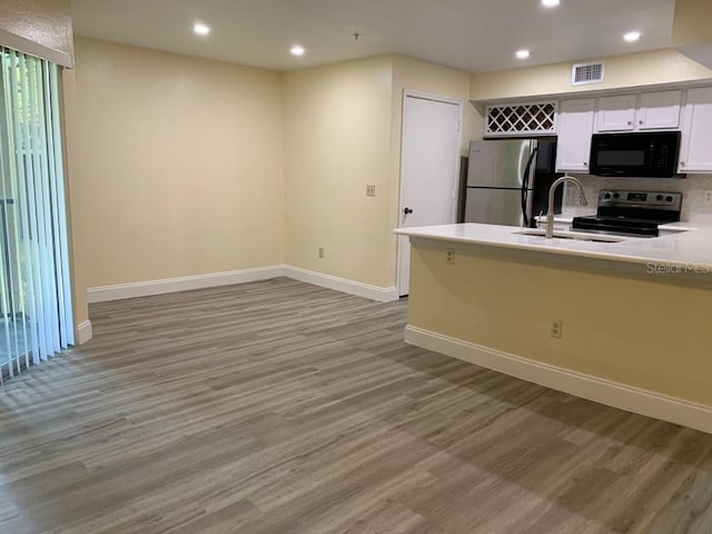 kitchen with stainless steel fridge, backsplash, range with electric cooktop, white cabinets, and light wood-type flooring