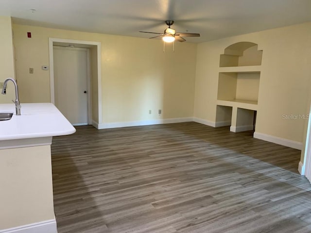 unfurnished living room featuring dark wood-type flooring, ceiling fan, sink, and built in features